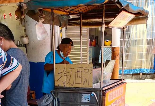 1名网友日前直击1名卖香肠的摊贩老板在人潮来往的大街上脱口罩抽菸，照片曝光后，还有人发现该摊贩的招牌竟写着「拎刀西郎」，嚣张语气吓坏不少人。（翻摄自脸书「路上观察学院」）