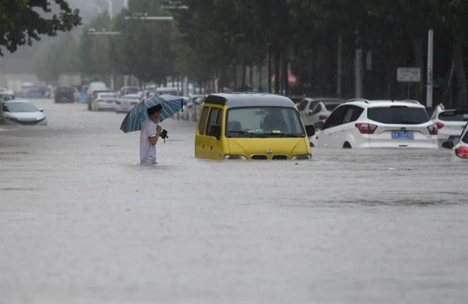 河南郑州强降雨，行人20日涉水通过积水路段。（大陆检察日报）