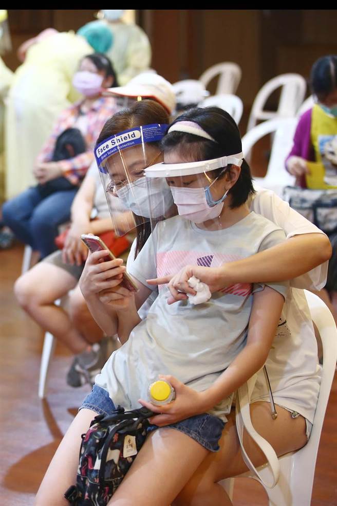 新北市教育局提醒境内所有国小教职员必须在8月中完成疫苗接种，22日有许多国小老师前往慈济中和静思堂施打站接种疫苗，一位妈妈带着小孩前往陪伴，打完疫苗后，小孩坐在妈妈的腿上，看着手机上的照片。（邓博仁摄）
