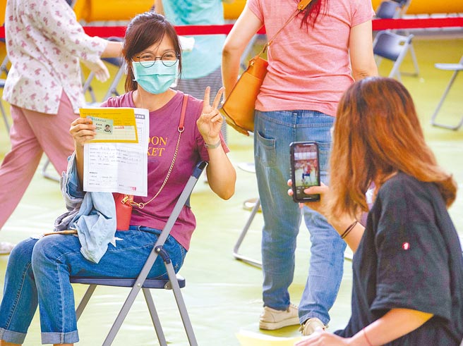 因應暑假後要開學，新北公私立國小教職員已陸續分流接種，聯合醫院21日在大觀國中設立接種站。一名教職員施打疫苗前，不忘請同事幫忙拍照，紀念難得的一刻。(羅永銘攝）