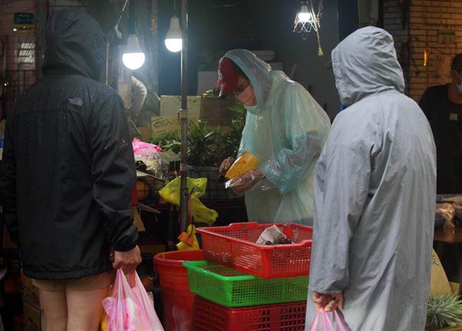 中央流行疫情指挥中心日前宣布7月27日到8月9日调降疫情警戒标准至第二级，市场取消身分证分流，摊商仍维持双罩一套，民眾24日在滨江市场冒雨购买蔬果。（张铠乙摄）
