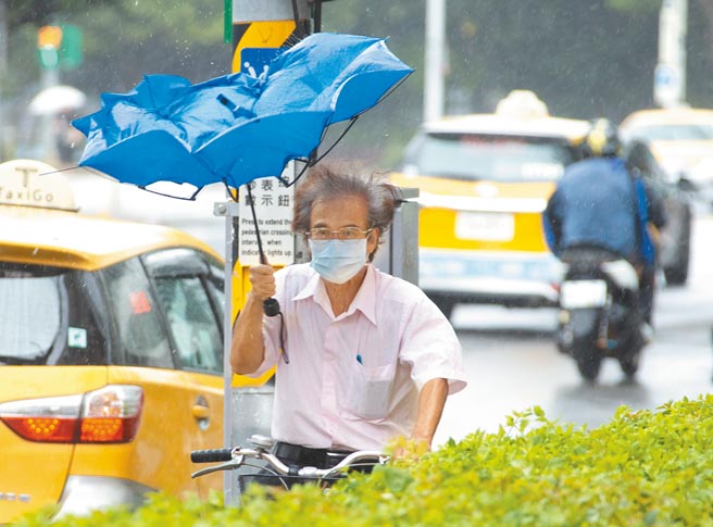 烟花颱風速度加快北轉，23日晚上8時到24日上午最接近台灣本島，有民眾騎車外出，手上雨傘被突如其來狂風吹翻。（羅永銘攝）