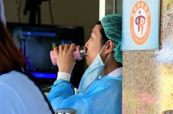 台东连续两天飙高温并且刮焚风，部东医院护理师在骑楼下穿着隔离衣值班，忍不住喝水解渴。（庄哲权摄）