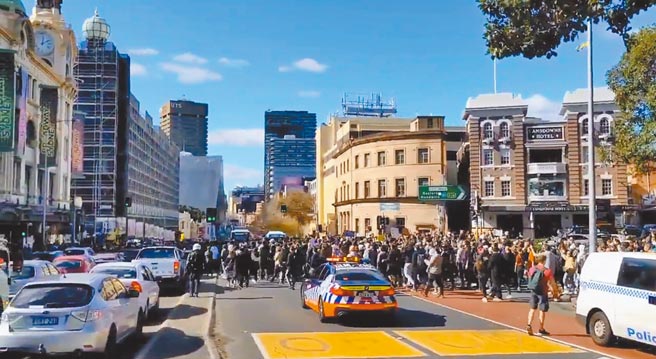 在澳洲雪梨，大批民眾24日走上街头，抗议政府实施严格的防疫措施。游行示威活动令道路为之受阻。（摘自推特影像画面）