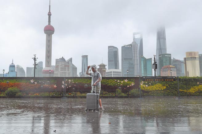 72年来7月最强的烟花颱风侵袭大陆，上海外滩江堤区域已拉起警戒线，临时关闭。图为一名游客在外滩冒雨行走。（中新社）