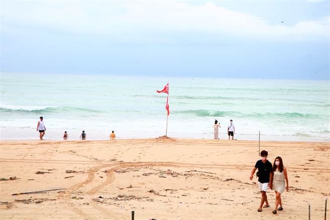 警戒降级首日南湾插红旗，但一早仍陆续出现游客，尤以亲子客居多，大手拉小手戏水玩得不亦乐乎。（谢佳潾摄）