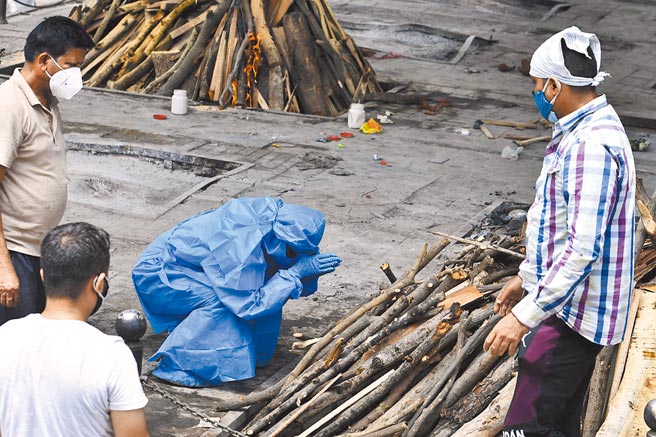 国际货币基金（IMF）27日警告，若任由新冠疫情在疫苗注射率偏低的穷国蔓延，2025年左右，全球产出恐损失约4.5兆美元（约台币126兆），而中低收入国家或承担三分之二以上的损失。图为印度新德里一家火葬场，一名身着防护服的亲属在火化前哀悼亲人。（新华社）