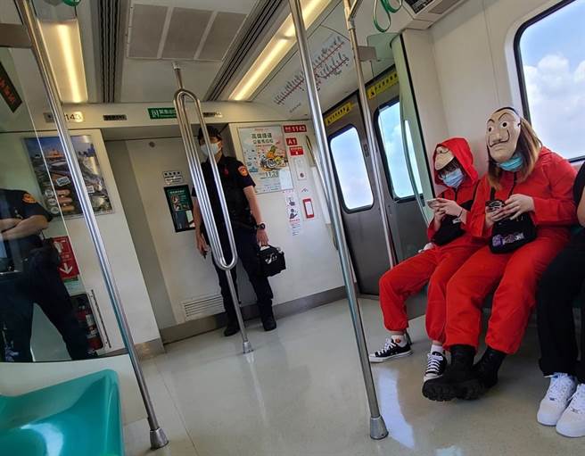 网友在捷运车厢内发现有2位民眾身穿美国影剧常见的「抢劫犯」服饰，而车厢内还有2名员警站在一旁，形成有趣的「警匪同车」画面。（翻摄自脸书「路上观察学院」）