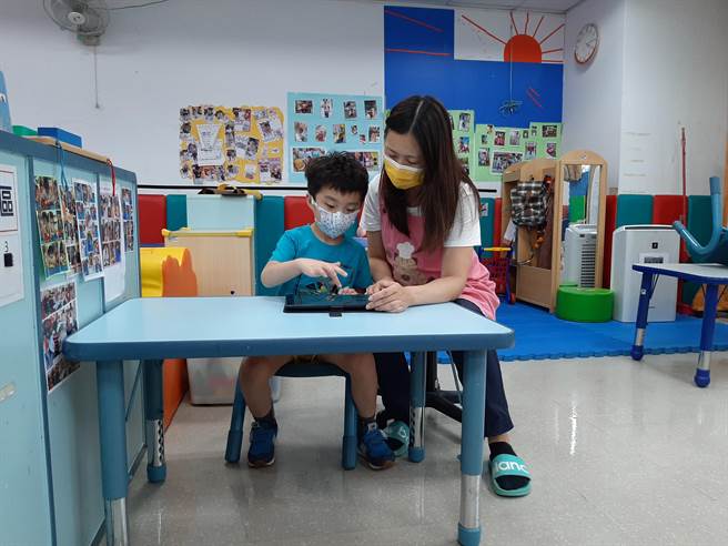 教保老師黃淑玲教小宇學習如何用平板電腦與人溝通。（社會局提供）