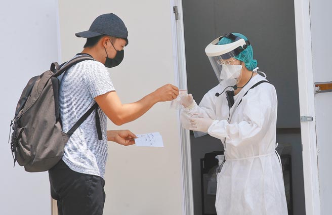 疫情指挥中心14日统计公布国内的境外移入个案中，共有12人完整接种满14天仍染疫。图为桃园机场一航厦外的筛检站，刚入境的旅客将唾液检体交给检疫人员。（范扬光摄）