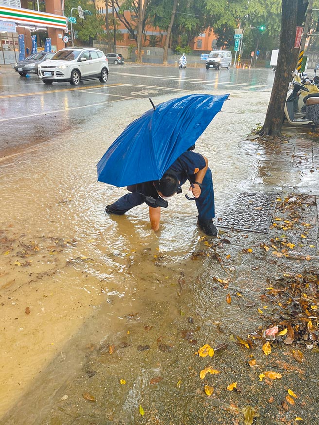 高雄地区14日清晨又下大雨，造成左营区文慈路与重爱路口道路积水，警方为排除积水，徒手挖通排水孔。（左营警分局提供／林雅惠高雄传真）