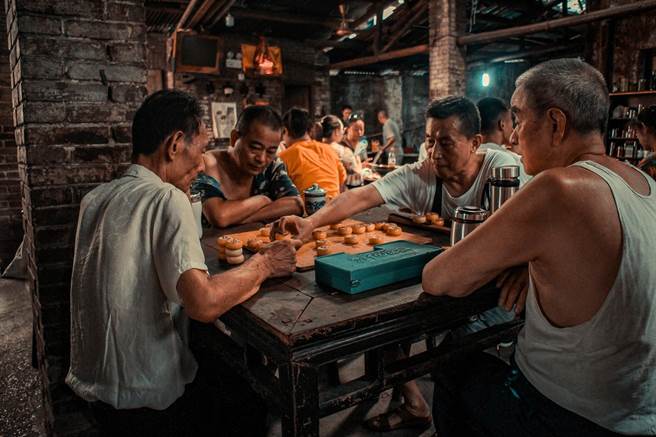 亞洲大學視傳系林駿騰拍攝「專注」系列作品之一，透過兩位民眾認真下棋、旁觀者凝神觀戰的構圖，呈現下棋者的「全神」與旁觀者的「貫注」。（亞大提供／林欣儀台中傳真）