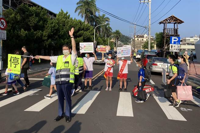 新竹县长杨文科穿反光背心，手持指挥棒，化身导护志工，在竹东镇中山国小护送学童上学。（罗浚滨摄）　
