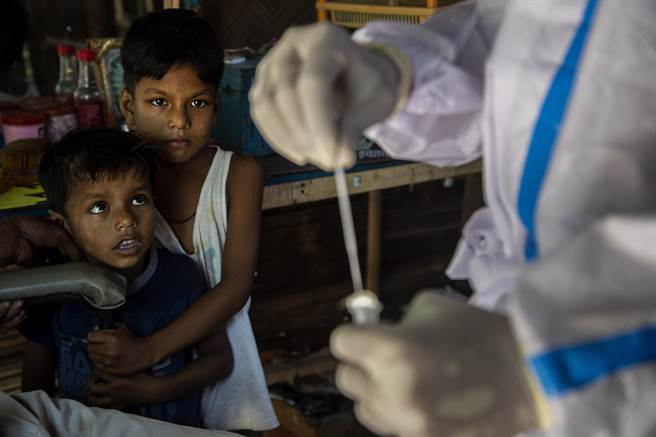印度当地儿童观看卫生人员採集COVID-19相关检体的情景。（美联社）