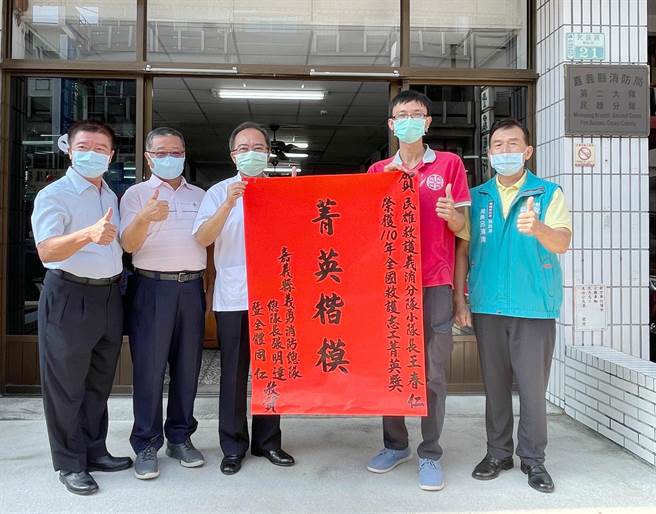 嘉县消防局长吕清海偕民雄乡乡长何嘉恒、救护义消大队长吕武锦等人前往民雄消防分队张贴红榜，向王春仁道贺。（嘉义县消防局提供∕吕妍庭摄）