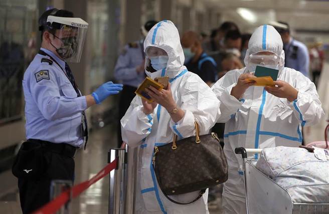 中央流行疫情指揮中心25日公布，國內新增5例新冠肺炎確定病例，均為境外移入，在桃園機場入境管制區內，防疫人員正協助身穿防護衣的旅客，上網登錄入境健康資料。（范揚光攝）
