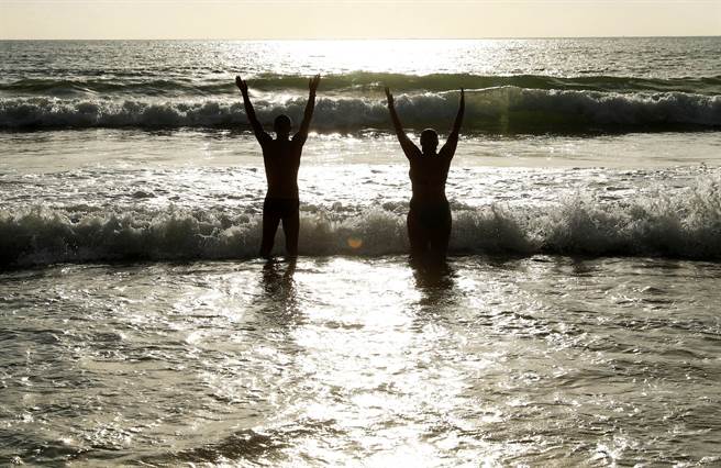 一對旅客在泰國普吉島的海邊高舉雙手。（圖／路透）