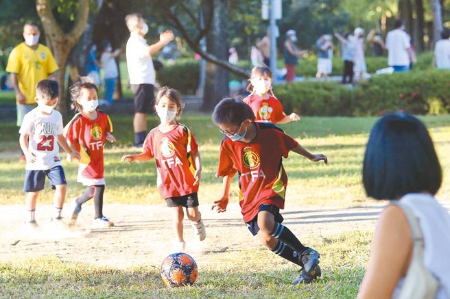 国内疫情趋缓，疫情指挥中心3日宣布，在户外空旷、人流较少的地方，将适度松绑戴口罩政策。图为小朋友戴口罩在公园踢足球。（陈俊吉摄）