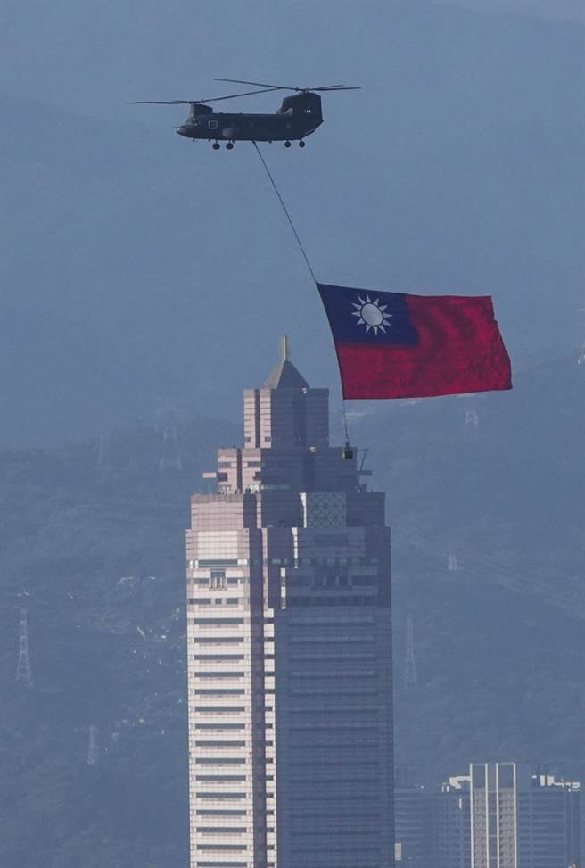 陆军契努克（CH-47SD）直升机吊挂国旗飞越台北市区，背景为台北车站前新光三越大楼。（黄子明摄）