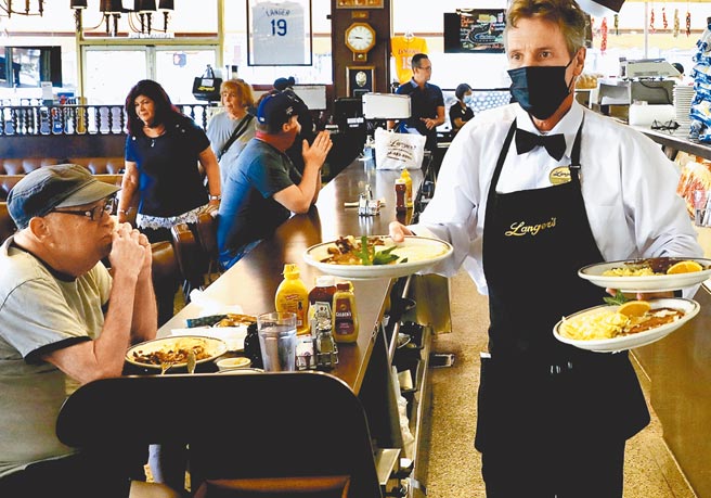 美國加州洛杉磯一家餐廳內，服務人員正在將餐點送到食客桌上。洛杉磯市議會通過新法令，規定成年顧客進入餐廳、酒吧、咖啡館、健身房、購物中心、博物館、電影院等室內公共場所，必須出示完成接種新冠疫苗的證明。（新華社資料照片）