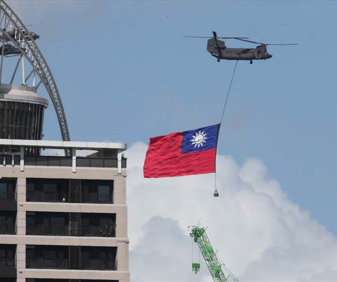 AH-64E阿帕契直升机、AH-1W超级眼镜蛇直升机护卫下，陆军契努克运输直升机吊挂史上最大型国旗进场。（陈君玮摄）