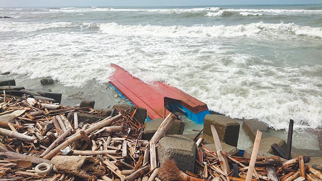 在台南市二仁溪出海口翻覆的动力舢舨船被强浪冲回岸边。（程炳璋摄）