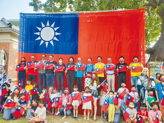 云林县府今年首度举行国庆日升旗典礼，10日在虎尾镇云林布袋戏馆旁升起巨幅国旗，升旗完后，民眾开心与国旗合照。（周丽兰摄）