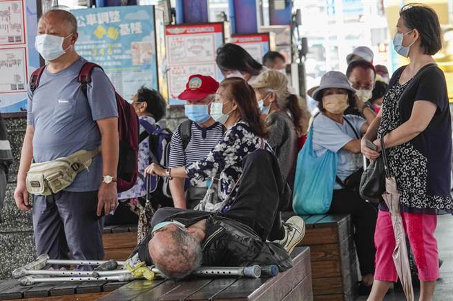 国内防疫措施虽已再度微解封，但大部分国人在公共场合仍习惯戴上口罩，基隆市区一处大型公车站上午聚集许多乘客候车，一名躺在座位上睡觉的长者也不忘戴着口罩。（黄子明摄）