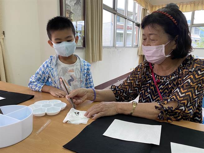 大埔樂齡中心國畫班阿嬤詹碧霞拿毛筆畫圖，小朋友看得有趣。（廖素慧攝）