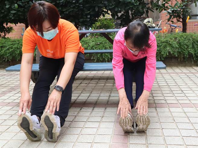 在弘道老人福利基金会照顾秘书开导下84岁林奶奶开始进行居家趣味运动课程，照顾秘书协助林奶奶做弯腰拉筋运动。（弘道老人福利基金会提供／冯惠宜台中传真）