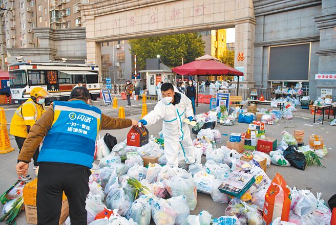 北京升高防疫措施，多場會議和論壇延期，馬拉松賽延後舉行，要求在京人員近期非必要不出京、按75％限流開放景區。圖為北京昌平區外賣配送員將貨物交給疫情防控人員。（新華社）