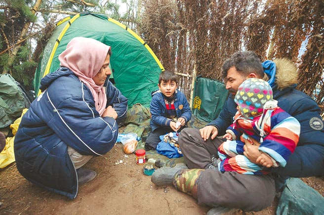 在白羅斯靠近波蘭邊境一處臨時搭建的營地，一個中東難民家庭在帳篷外用餐。隨著天氣轉寒，白羅斯總統盧卡申科下令白國軍方在邊境設置帳篷，並讓難民能取得糧食和其它人道救援物資。（美聯社）