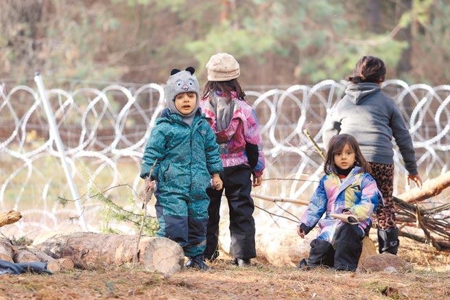 幾名難民小孩在白羅斯和波蘭邊界的鐵網圍籬前聚集玩耍。（路透）
