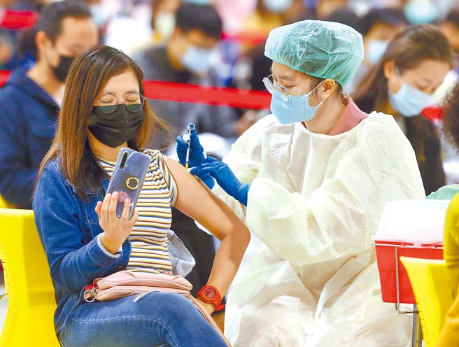 第15轮开放3大疫苗施打，并开放混合接种，25日有许多民眾前往北市花博接种站，一位民眾在注射时拿起手机自拍。（粘耿豪摄）