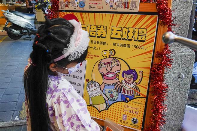 迪化商圈為振興商機，29日宣告12月「秋穫季」起跑，推出「神農香囊」，搭配100家店家的熊好券、振興券優惠，商圈一家業者設計精美振興五倍券海報，吸引小女孩駐足觀看。（黃子明攝）
