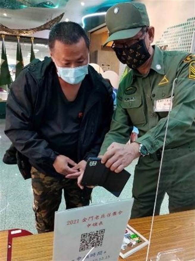 老兵志工林启谈（右）在尚义机场老兵召集令活动接待柜台执勤，协助返金老兵填写资料。（金门县府观光处提供）