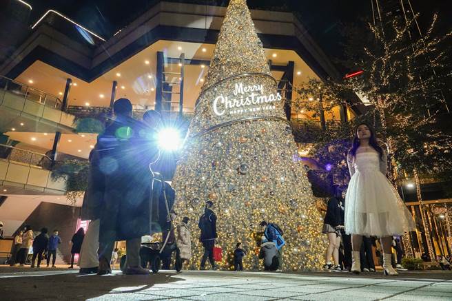 台北市信義區人行步道區設置大型耶誕樹，一名女孩穿著白色洋裝拍照打卡。（黃子明攝）