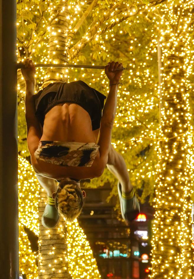 一名男子吊掛在台北市信義區LED燈飾旁的路燈燈柱上玩翻滾遊戲。（黃子明攝）