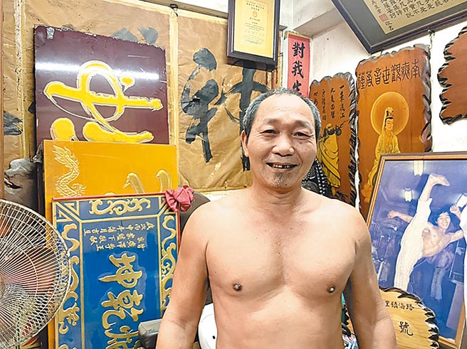 在高雄鳳山區三民路上，打赤膊的吳崑章手握刻刀，專注地在木匾上來來回回刻畫著。（洪靖宜攝）
