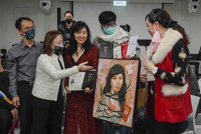 完成受洗的女性教友拿著同時受洗的丈夫所繪畫像，與牧師及教友留影紀念。（黃子明攝）