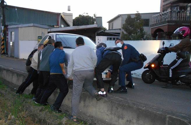 王女駕駛銀色轎車，會車時不慎前輪掉落田埂，霧峰分局大里分駐所員警號召民眾，一起將右前輪抬回路上。（霧峰分局提供／黃國峰台中傳真）