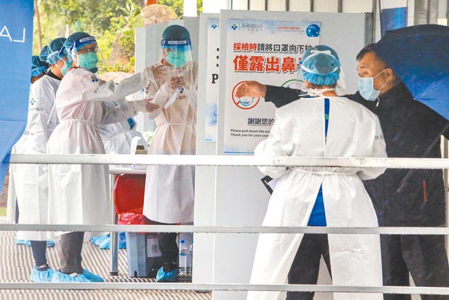 疫情指挥中心昨宣布，北市再增1起防疫旅馆群聚案。图为忠贞市场附近採检站医护人员调整好防护衣装备，再开始为排队民眾登记资料。（陈麒全摄）