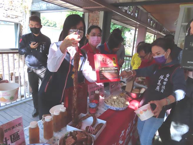 水交社年货大街宣布开跑，南区区长萧琇华（提香肠者）与台南市议员林美燕、周丽津等人，体验水交社传统商家的美食。（台南市区公所提供／程炳璋台南传真）