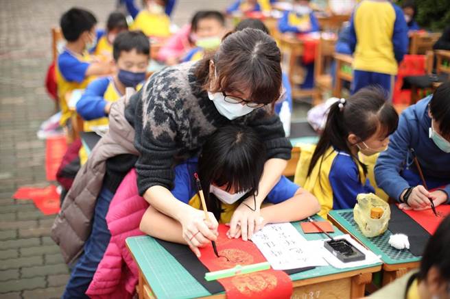 嘉义市育人国小全校师生现场挥毫写春联，老师扶着小朋友一笔一画教写。（嘉义市政府提供）