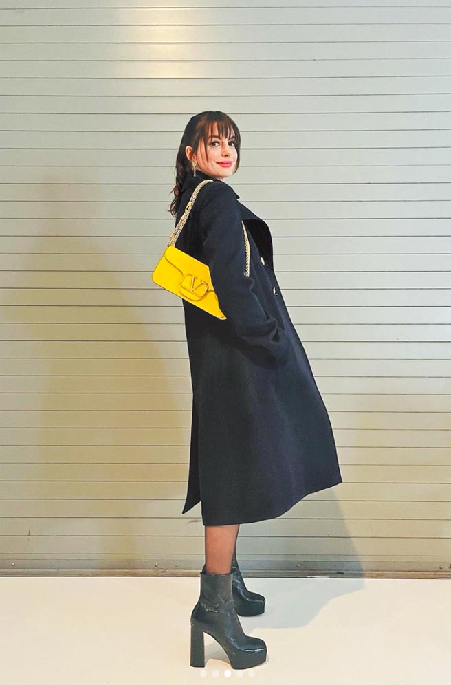 安海瑟薇连身裤外搭黑色大衣，造型以Valentino Garavani Loco’ 柠檬黄肩背包画龙点睛，包7万8500元。（摘自安海瑟薇IG）