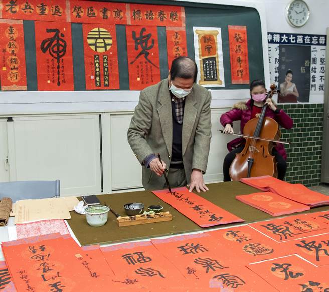 「将军书法家」郑有谅在孙女黄莘宁的大提琴悠扬乐声伴奏下，挥毫写下气势磅礡的战地春联。（金门县林务所提供）