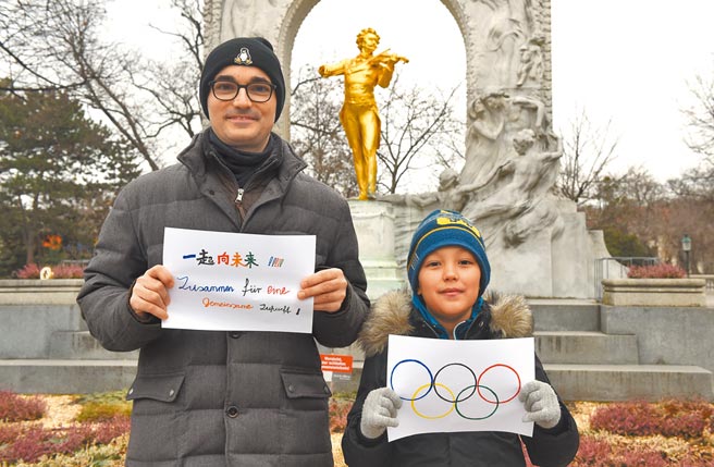 《纽约时报》指出，从2008年北京奥运到2022年冬奥，中国已不再需要证明自己在世界舞台上的地位外，也无视那些批评者。图为奥地利维也纳一对父子手持「一起向未来」的主题口号和奥运五环标志，祝福北京冬奥会。（新华社）