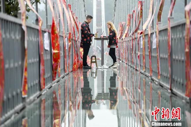 2019年1月，湖南长沙石燕湖玻璃桥上贴满了春联，两名外籍游客在玻璃桥上学习写春联。（图/中新社）