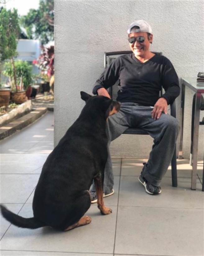 梁家辉坐在庭院里逗狗的样子，看上去十分开心。（图／截取自微博）