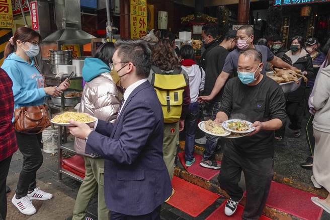 金山老街挤满人潮，民眾涌入知名美食店家品尝佳肴，由于店家厨房与餐席分离，饕客端着菜肴穿梭人群中前往老街多处店面享用。（黄子明摄）